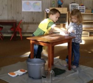 One child scrubs a table while another observes.
